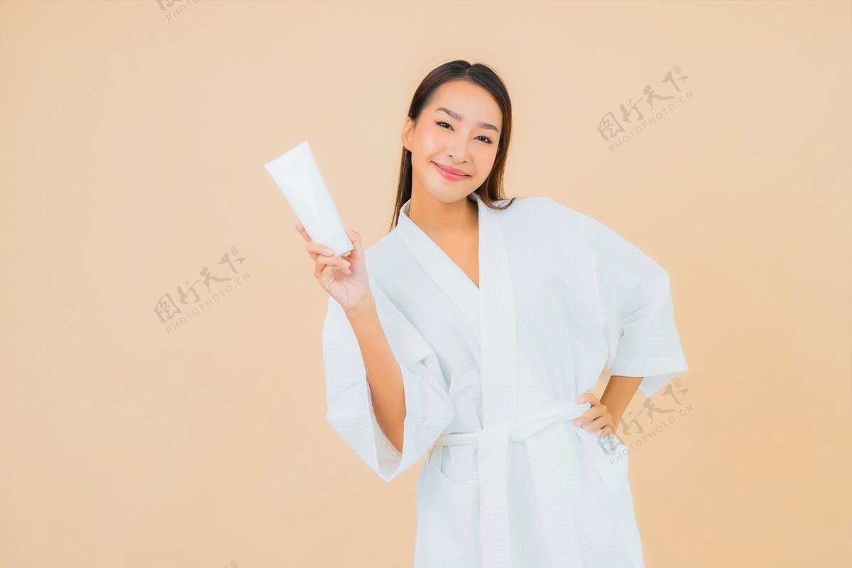 女人肖像美丽的亚洲年轻女子与瓶乳液和面霜米色向上中国人美白