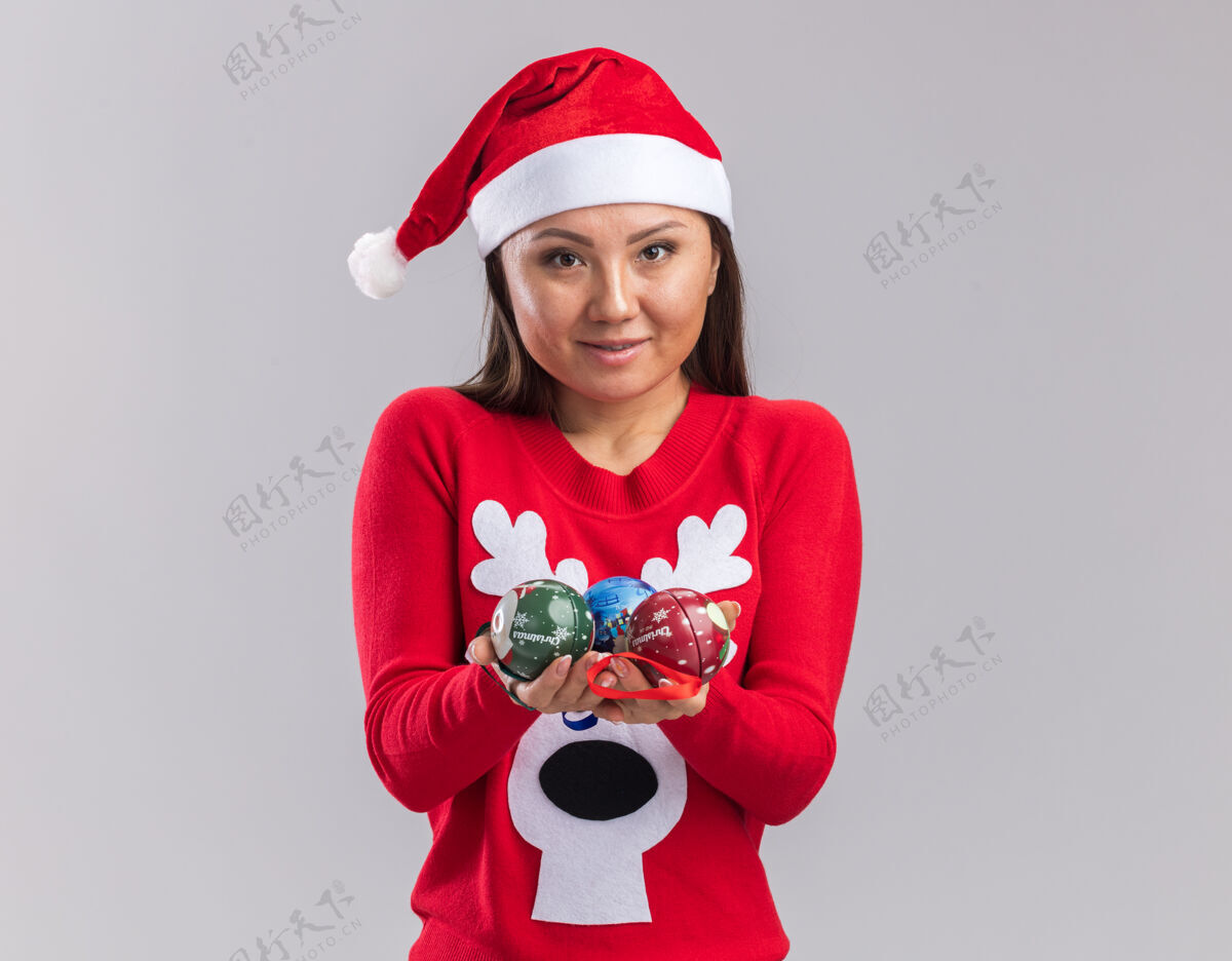 女孩高兴的年轻亚洲女孩戴着圣诞帽和毛衣举行圣诞树球在镜头隔离在白色背景树高兴举行