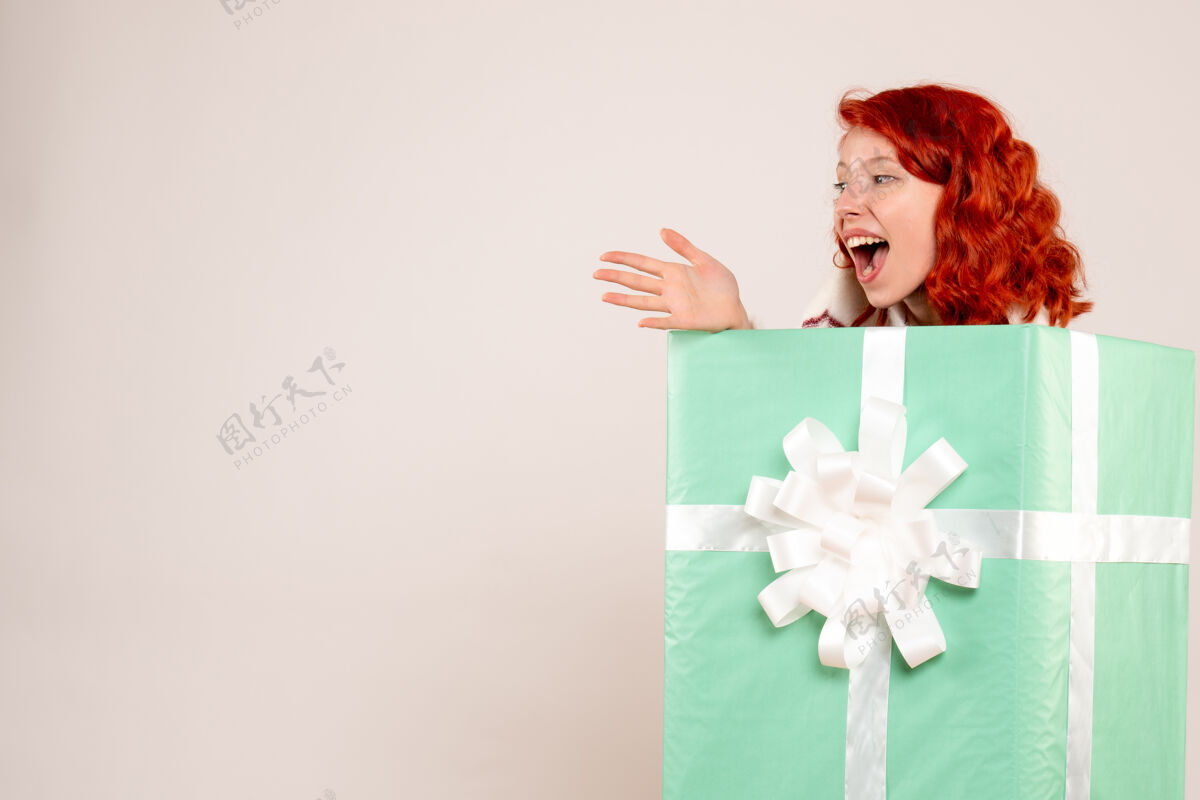 礼物隐藏在白墙上的年轻女子的正面视图节日快乐女性