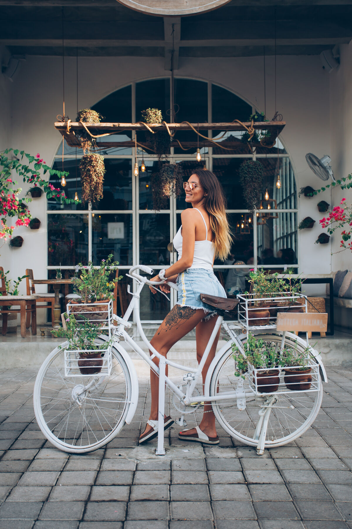 休息穿着牛仔裤短裤和白色上衣的可爱的纹身白人妇女站在街边咖啡馆的背景下骑自行车咖啡自行车骑自行车