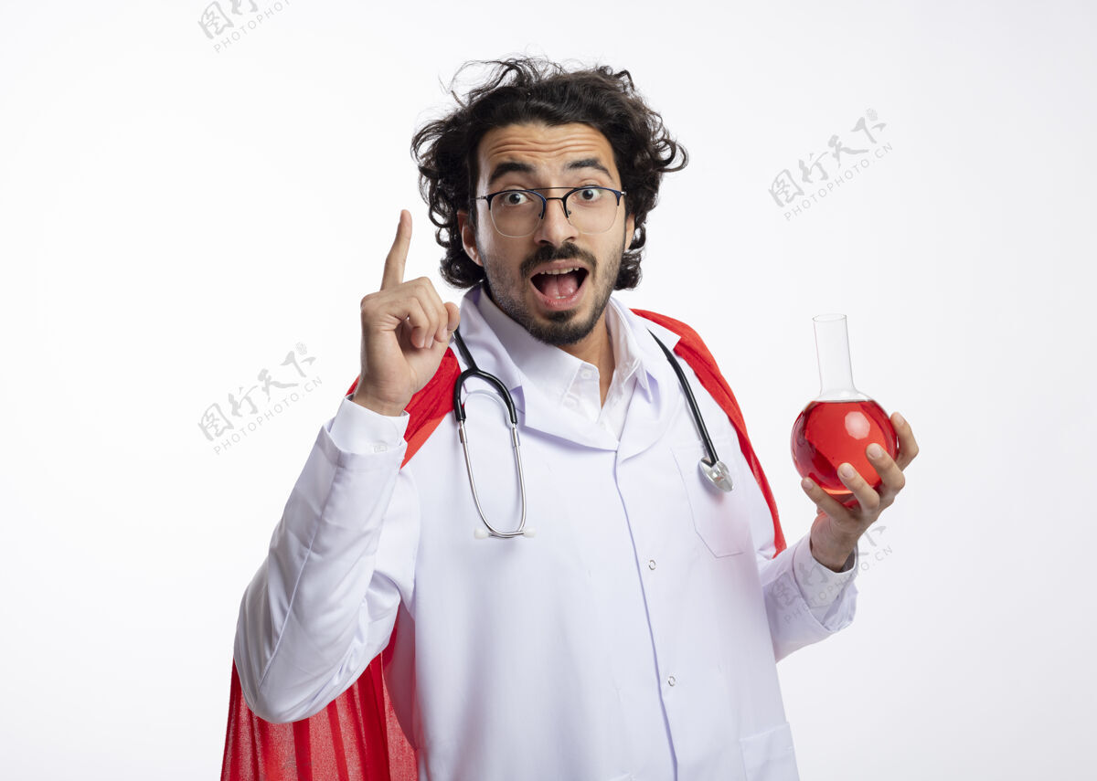 穿着年轻的白种人超级英雄戴着眼镜 身穿医生制服 披着红色斗篷 脖子上戴着听诊器 手里拿着玻璃瓶里的红色化学液体 指着上面烧瓶超级英雄男人