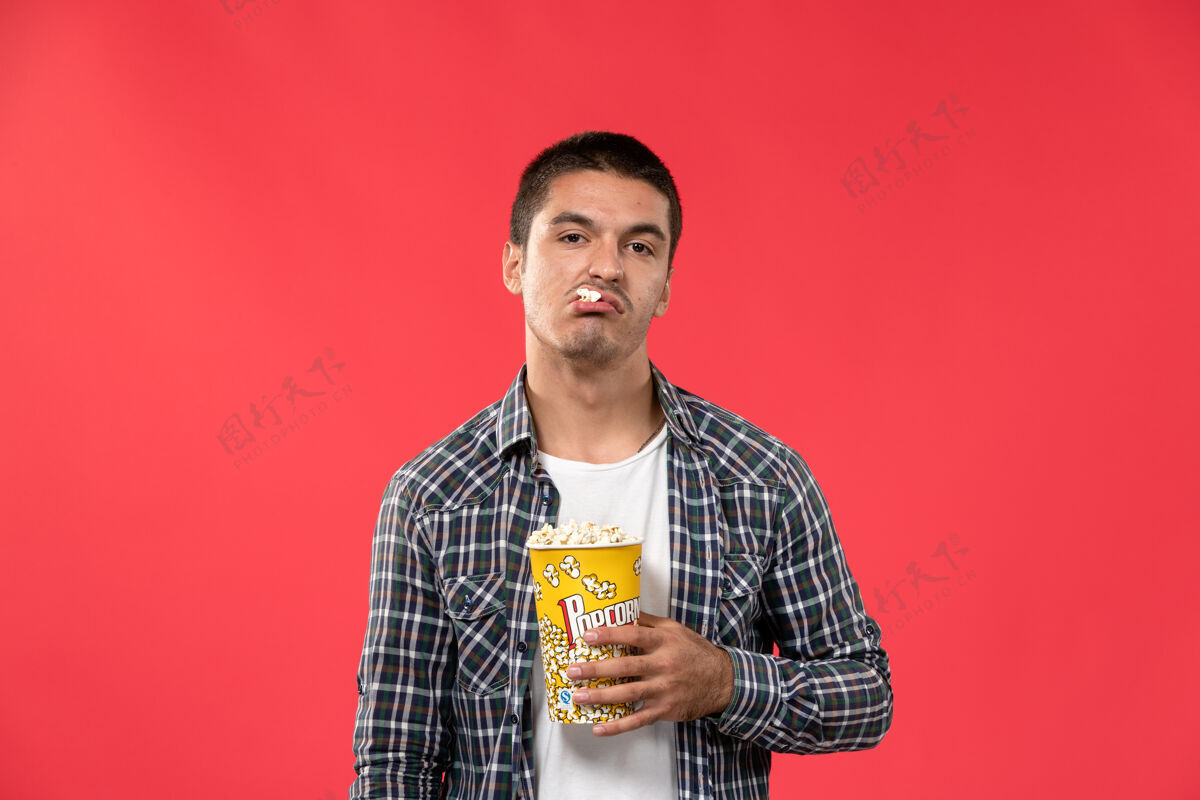 男性正面图年轻男子拿着爆米花包在浅红的墙上看电影剧院肖像西装