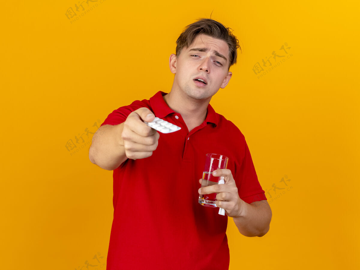 餐巾印象深刻的年轻英俊的金发病男子手持一包药片一杯水和餐巾包金发水