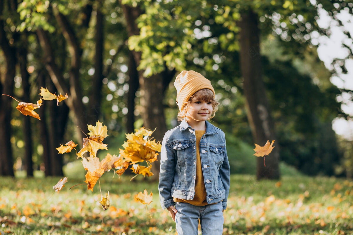 甜蜜可爱的小男孩在秋天公园玩树叶卷发黄色帽子小男孩