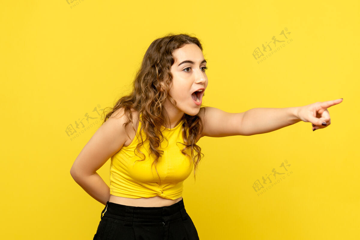 年轻年轻女子指着黄色墙壁的正视图头发指向女性