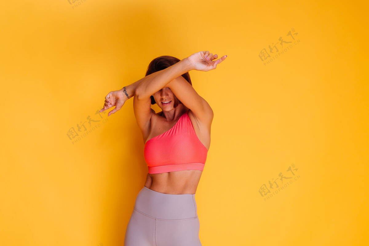 锻炼年轻健壮的女人穿着运动服 时髦的上衣和紧身裤 对着黄色的墙壁摆姿势腹部臀部成人