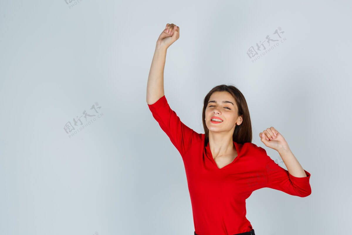 自由穿着红色上衣的年轻女士 裙子显示出赢家的姿态 看起来很幸福幸福海滩手势