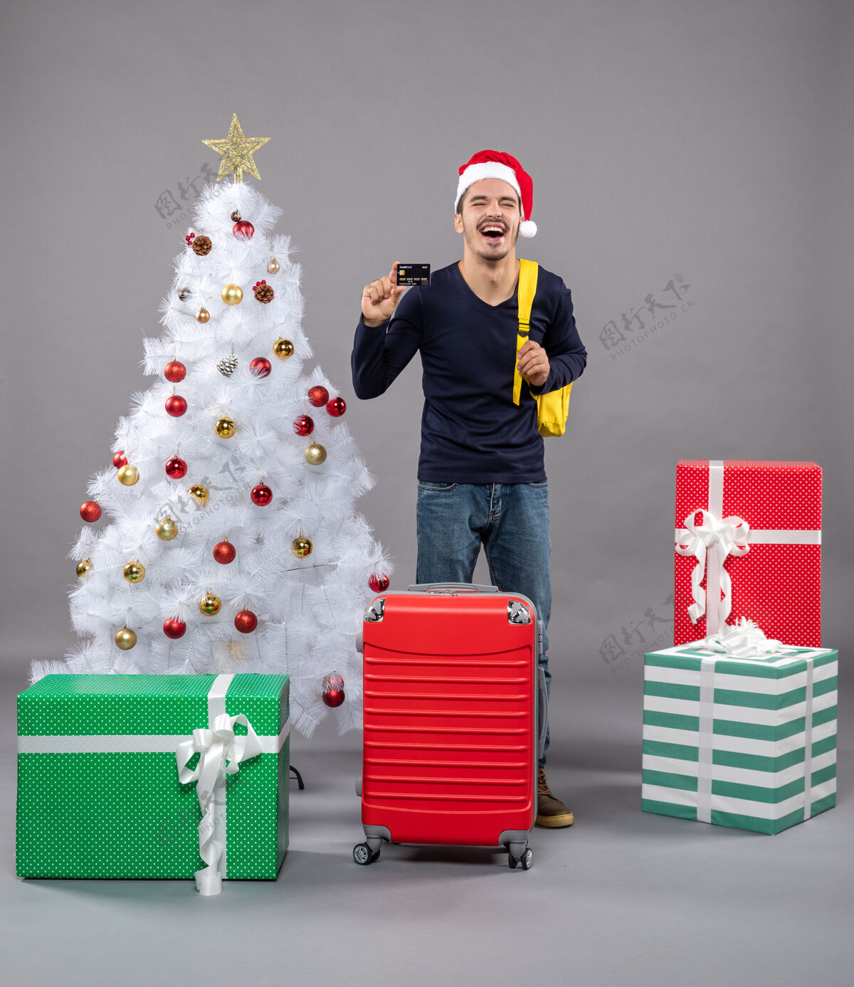 袋子一个拿着卡片的年轻人笑着站在圣诞树旁 孤立无援圣诞树礼物商店