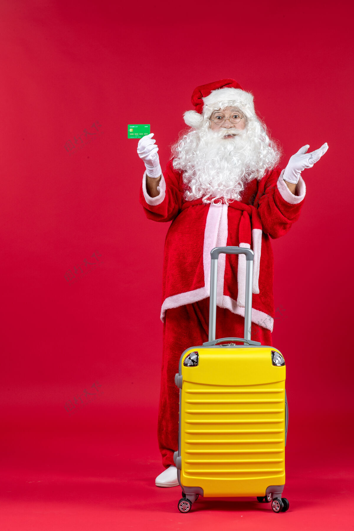 男人红墙上拿着绿色银行卡的黄色袋子的圣诞老人的正视图举行圣诞老人庆祝