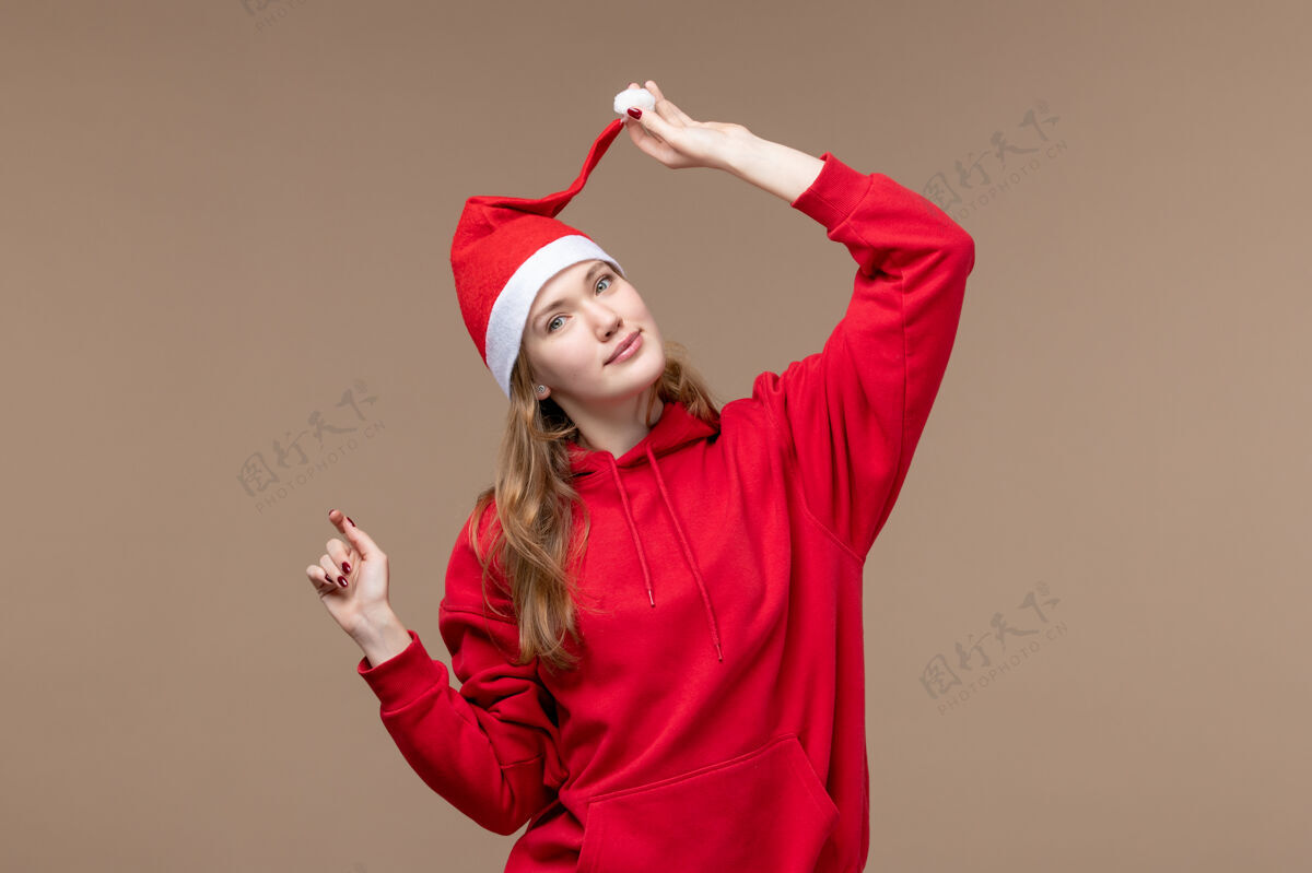 节日正面图：棕色背景下 年轻女性带着红色斗篷微笑着过圣诞节年轻女性美丽红色