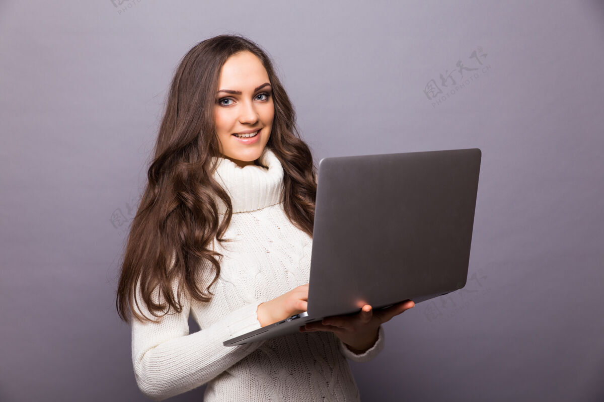 笔记本电脑一个快乐的惊讶的女人站在灰色的墙上 笔记本电脑被隔离女人打字休闲