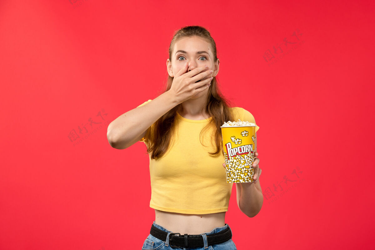 音乐家正面图年轻女性在电影院拿着爆米花包 表情震惊的红墙电影院小吃好玩的电影电影院爆米花电影
