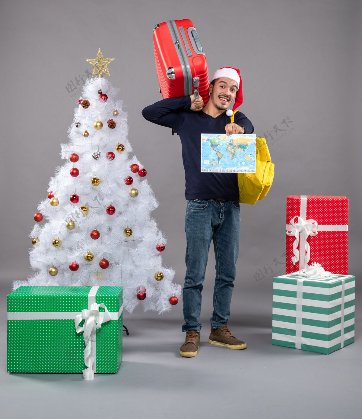 圣诞树带着黄色背包的微笑男人拿着地图在灰色的圣诞树旁圣诞树圣诞老人圣诞老人帽子