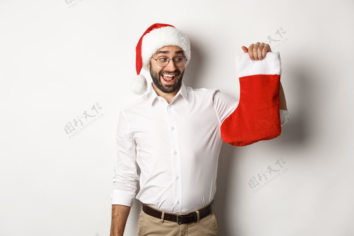 圣诞节圣诞快乐 节日概念快乐的成年人收到礼物在圣诞节袜子 看起来很兴奋 戴着圣诞帽脸微笑西装