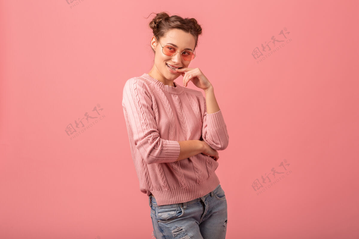 女性年轻漂亮的微笑调情女子在粉红色的毛衣和太阳镜孤立在粉红色的工作室背景粉色眼镜脸