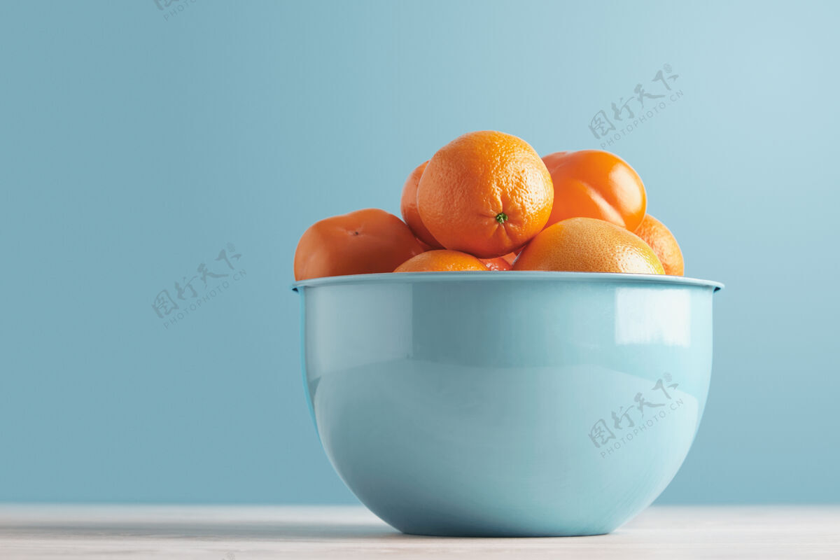 热带美味的新鲜水果和柠檬放在蓝色金属碗里 放在白色的图登桌子上 背景是柔和的蓝色：柿子 枣子 李子 柑橘 橘子 柚子 柚子饮食成熟日本