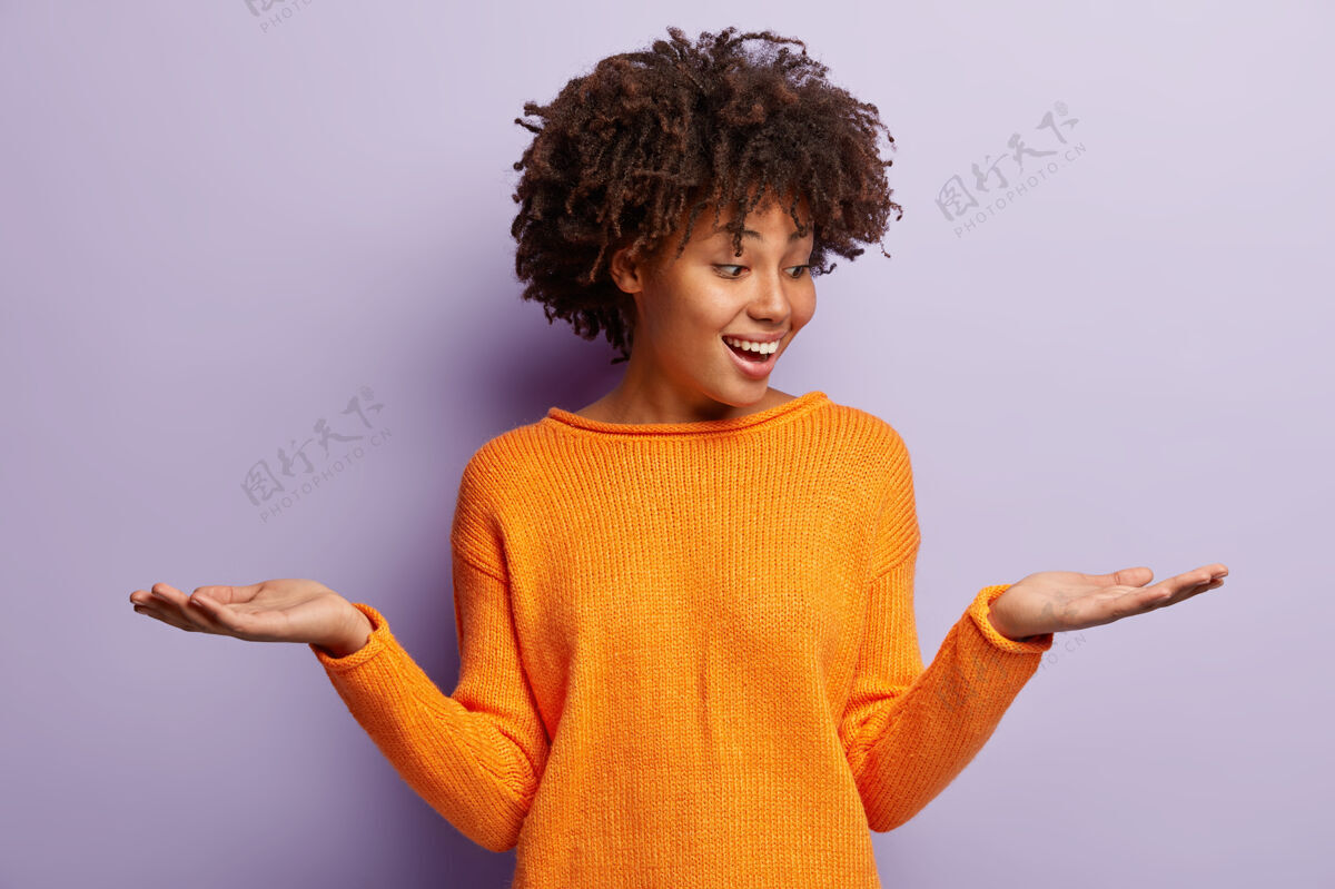 种族快乐乐观的非裔美国女人举起双手 假装拿着两件东西 心情很好 穿着休闲装 隔着紫色的墙满意的女人拿着复制空间肖像黑暗摆姿势