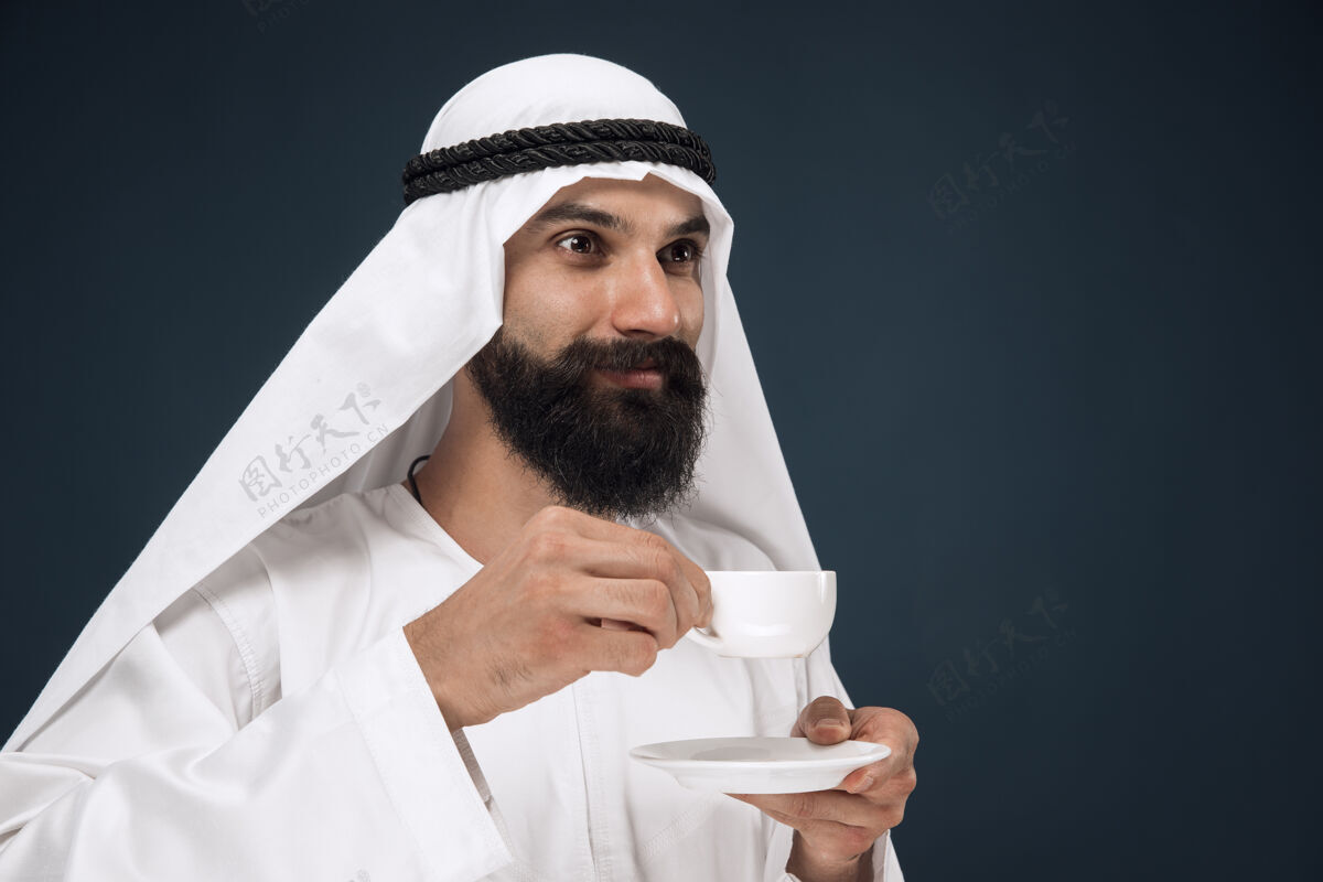 反应阿拉伯沙特男子肖像年轻的男模站着喝咖啡或茶人男孩穆斯林