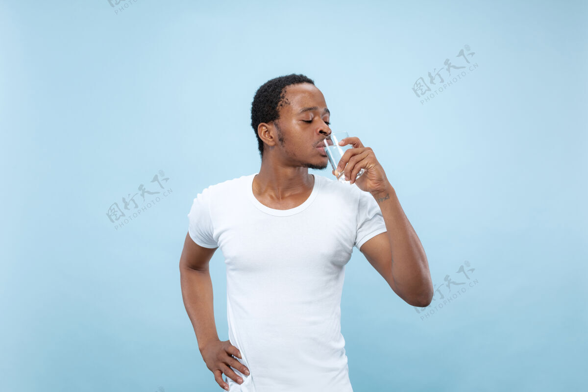 顺序一个穿着白衬衫的非洲裔美国年轻人的特写肖像…拿着一个杯子和饮用水男性英俊观点
