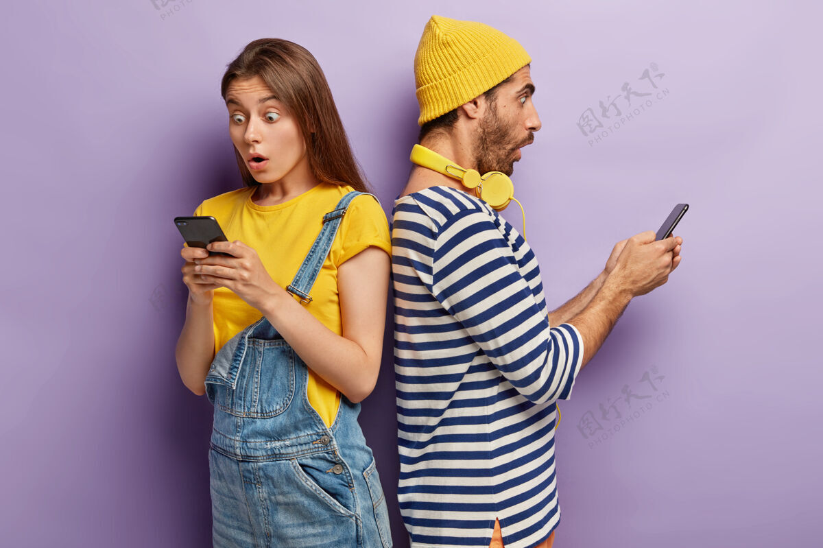 妻子震惊情绪的男青年和女青年站在回头 惊讶于坏消息 键入各种信息 感到印象深刻和震惊智能手机关系摆姿势
