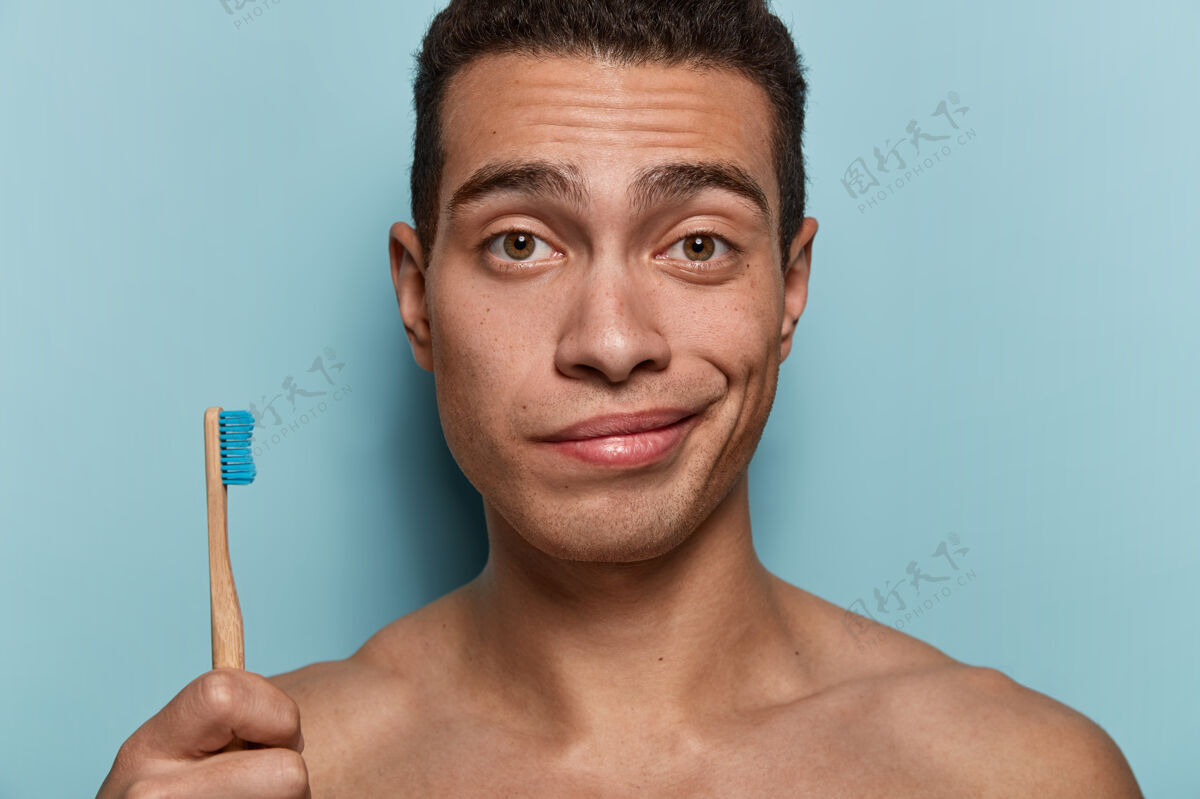 浴室皮肤健康 身体强壮 拿着牙刷 早上要做卫生程序 站在蓝色墙壁上的年轻人的特写镜头卫生 牙齿护理和美容概念卫生外观卫生
