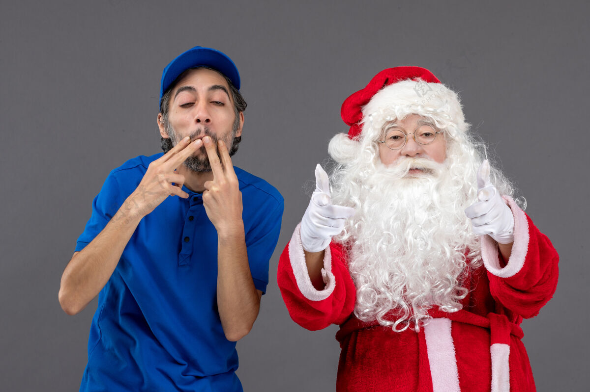 人灰色墙上的圣诞老人和男信使的正面图庆祝信使仪器