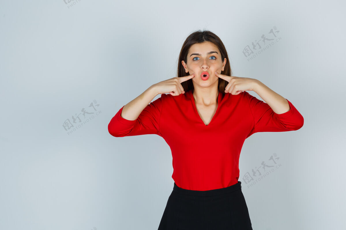 成人穿红衬衫的年轻女士 裙子把手指压在脸颊上人手指女人