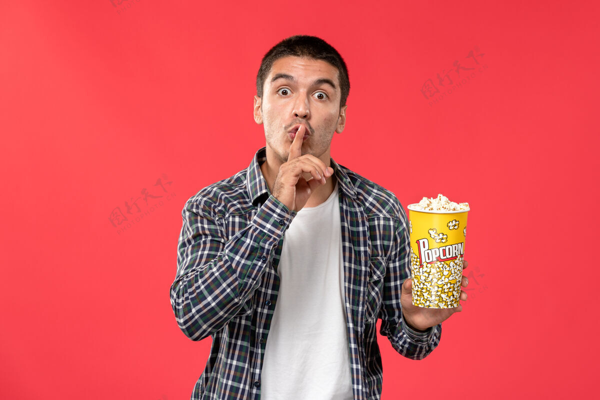 爆米花正面图年轻男子手持爆米花包在浅红墙电影院看电影艺人电影成年人