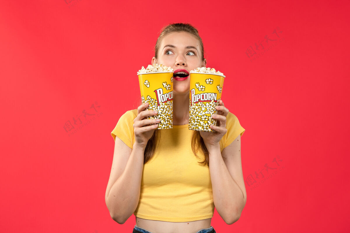 年轻人正面图年轻的女性在电影院拿着爆米花包在红墙电影院的电影院小吃女性趣味电影年轻女性微笑表情