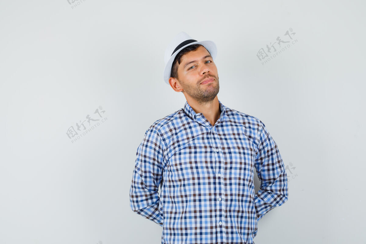 现代穿着格子衬衫 戴着帽子 双手放在背上的年轻人看起来很自信快乐自信休闲