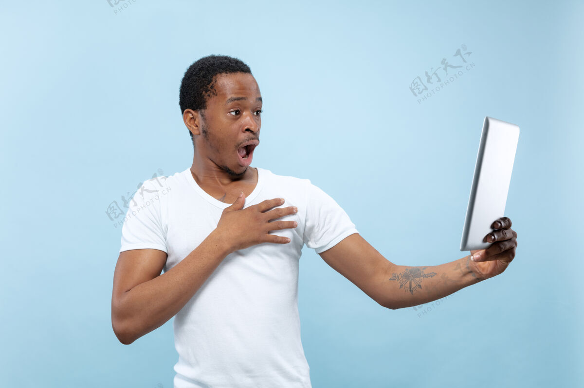 人穿着白衬衫的非洲裔美国年轻人的特写肖像人类情感 面部表情 广告 销售概念使用平板电脑 震惊自拍或虚拟博客男性顺序年轻