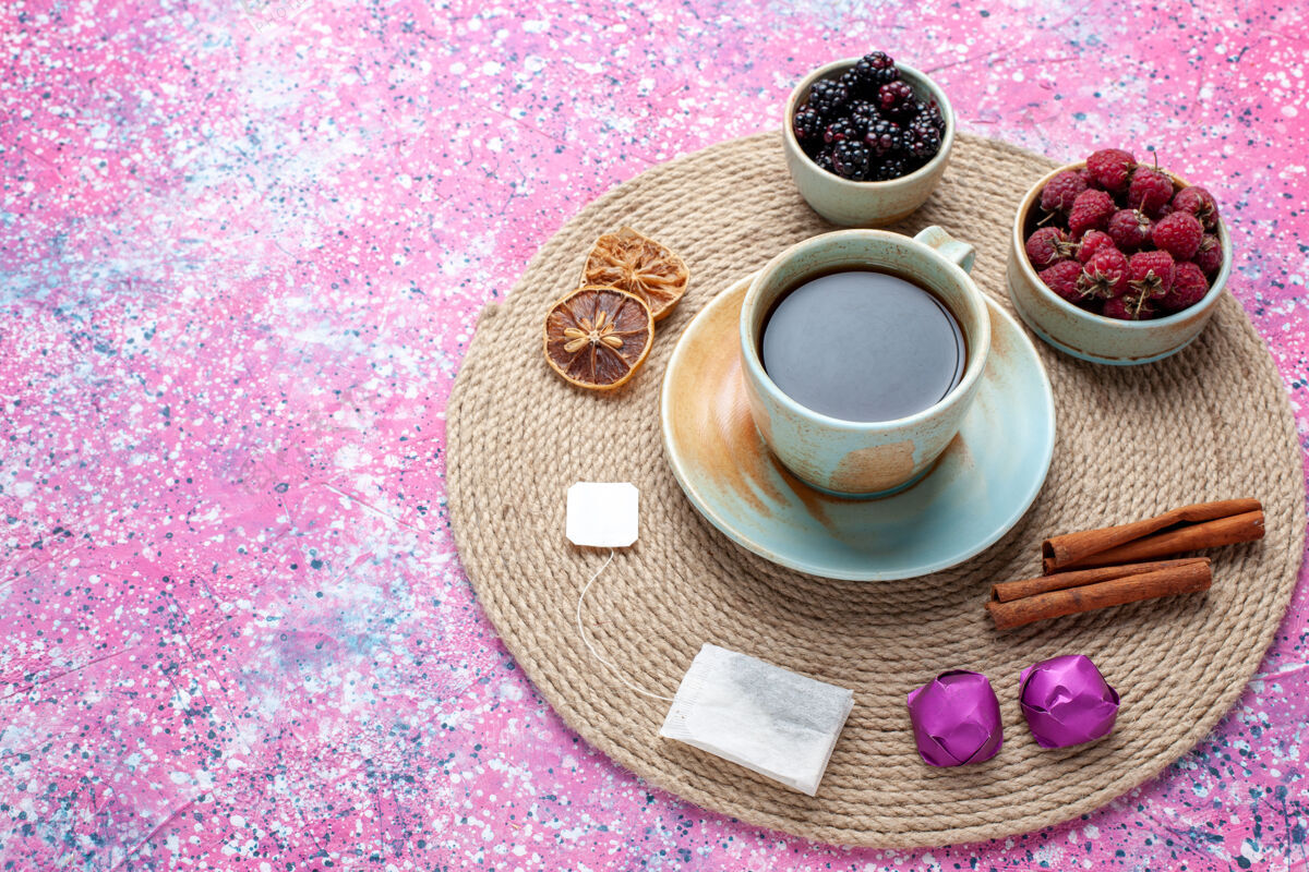 杯子半俯视新鲜浆果 覆盆子和黑莓 粉色书桌上放着茶和肉桂肉桂半顶茶