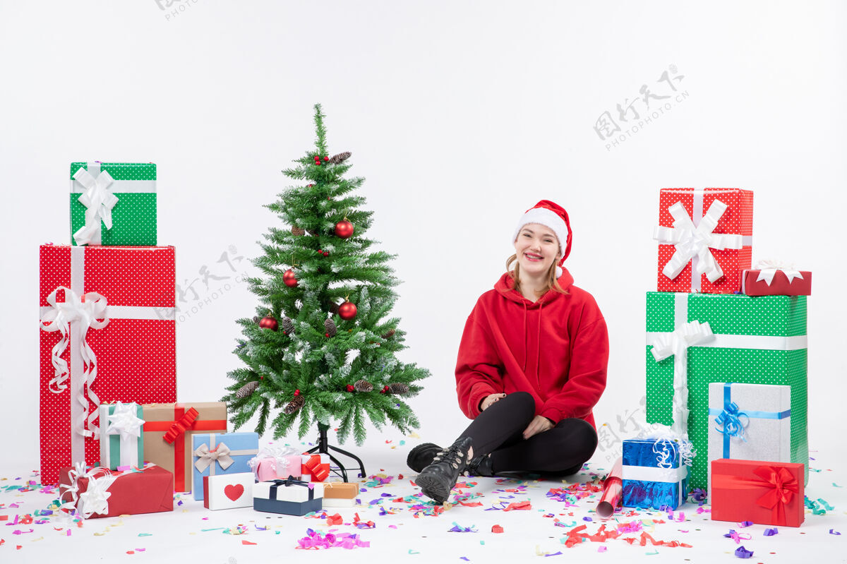 雪年轻女子坐在白色墙壁上的节日礼物周围的正面视图庆祝十二月人