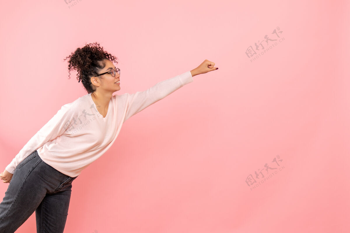 美丽年轻女子在粉红色墙上摆超人姿势的正面图年轻女性年轻生活方式