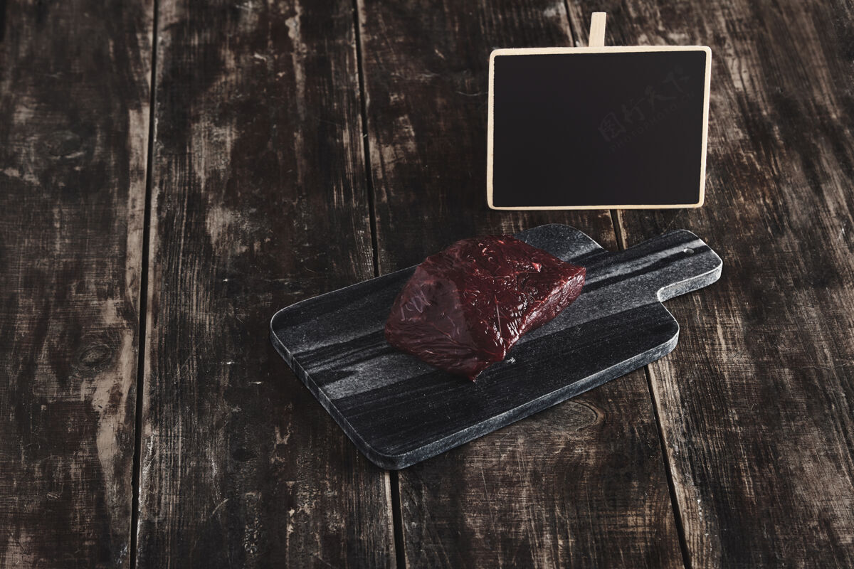 熟食店侧视图豪华生鱼排片在黑色大理石切割桌和老古董木表和黑板价格标签狩猎肉血