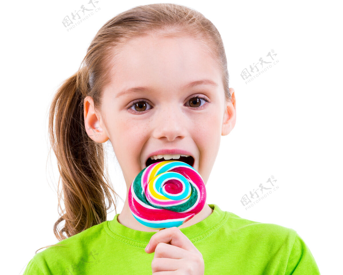 休闲微笑的小女孩穿着绿色t恤 吃着彩色糖果-白色隔离糖果美丽积极