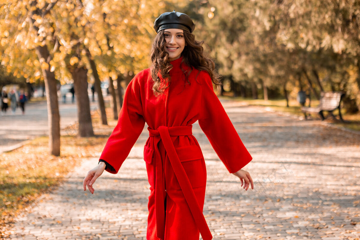 阳光迷人的时尚微笑的女人卷发漫步在公园穿着温暖的红色外套秋季时尚 街头风格 戴贝雷帽时尚女士秋天