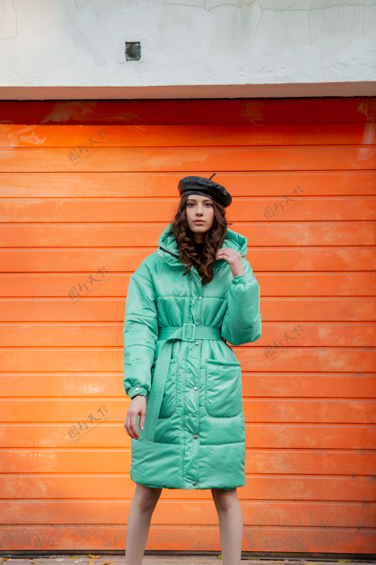 泡芙穿着冬秋时尚潮流蓬松外套和帽子贝雷帽的时髦女人在街上对着橙色的墙壁摆姿势户外漂亮夹克