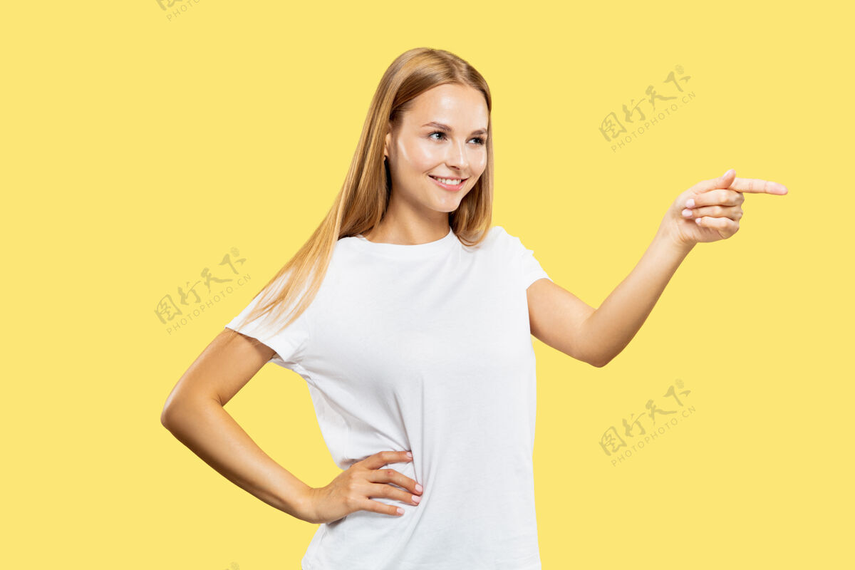 手黄色工作室背景上的白人年轻女子半身像穿着白衬衫的漂亮女模特人类情感的概念 面部表情侧指微笑表情金发专业