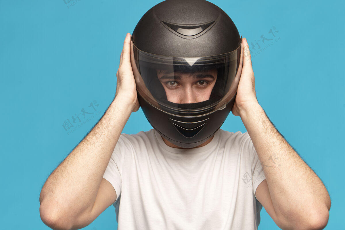 汽车独立工作室拍摄的自决认真的年轻白人男性骑自行车的时尚黑色摩托车头盔摩托车休闲服装