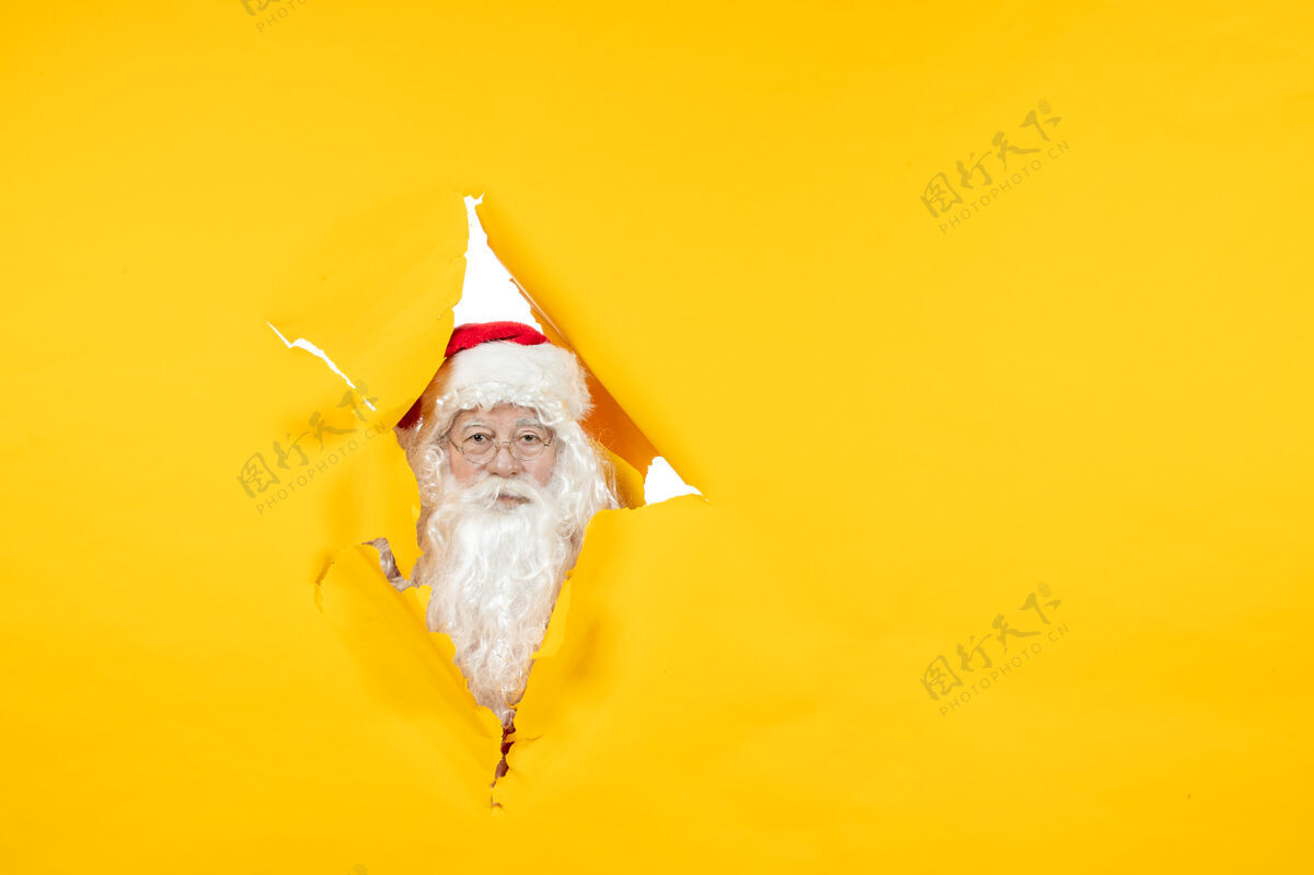 庆祝圣诞老人透过撕破的黄色墙壁看的正视图十二月看节日