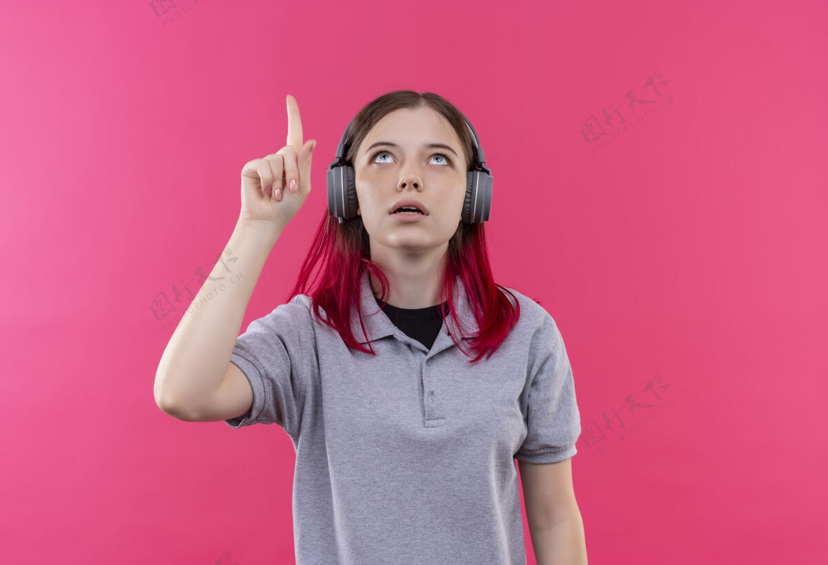 T恤看着上了年纪的漂亮女孩戴着灰色t恤戴着耳机手指向上点着孤立的粉色背景向上耳机女孩