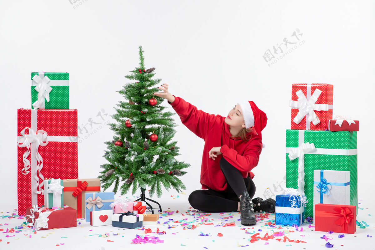 节日年轻女子坐在白色墙壁上的节日礼物周围的正面视图圣诞季节十二月