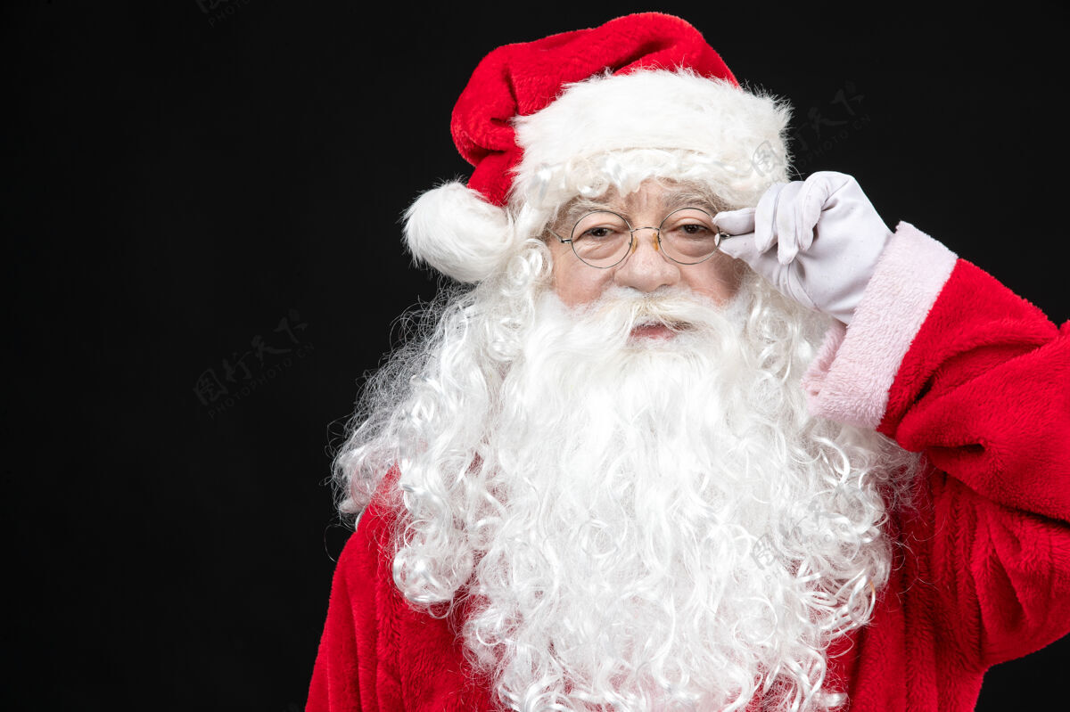 服装圣诞老人穿着经典的红色套装 留着白胡子 站在黑色的墙上快乐圣诞老人站立