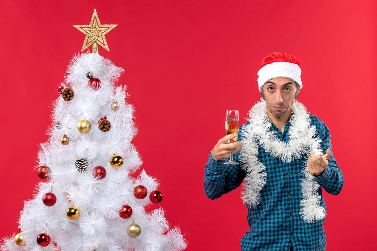 红色圣诞节心情与悲伤的年轻人圣诞老人帽子在一个蓝色的衬衫剥离举行一杯葡萄酒附近圣诞树新年圣诞老人白色