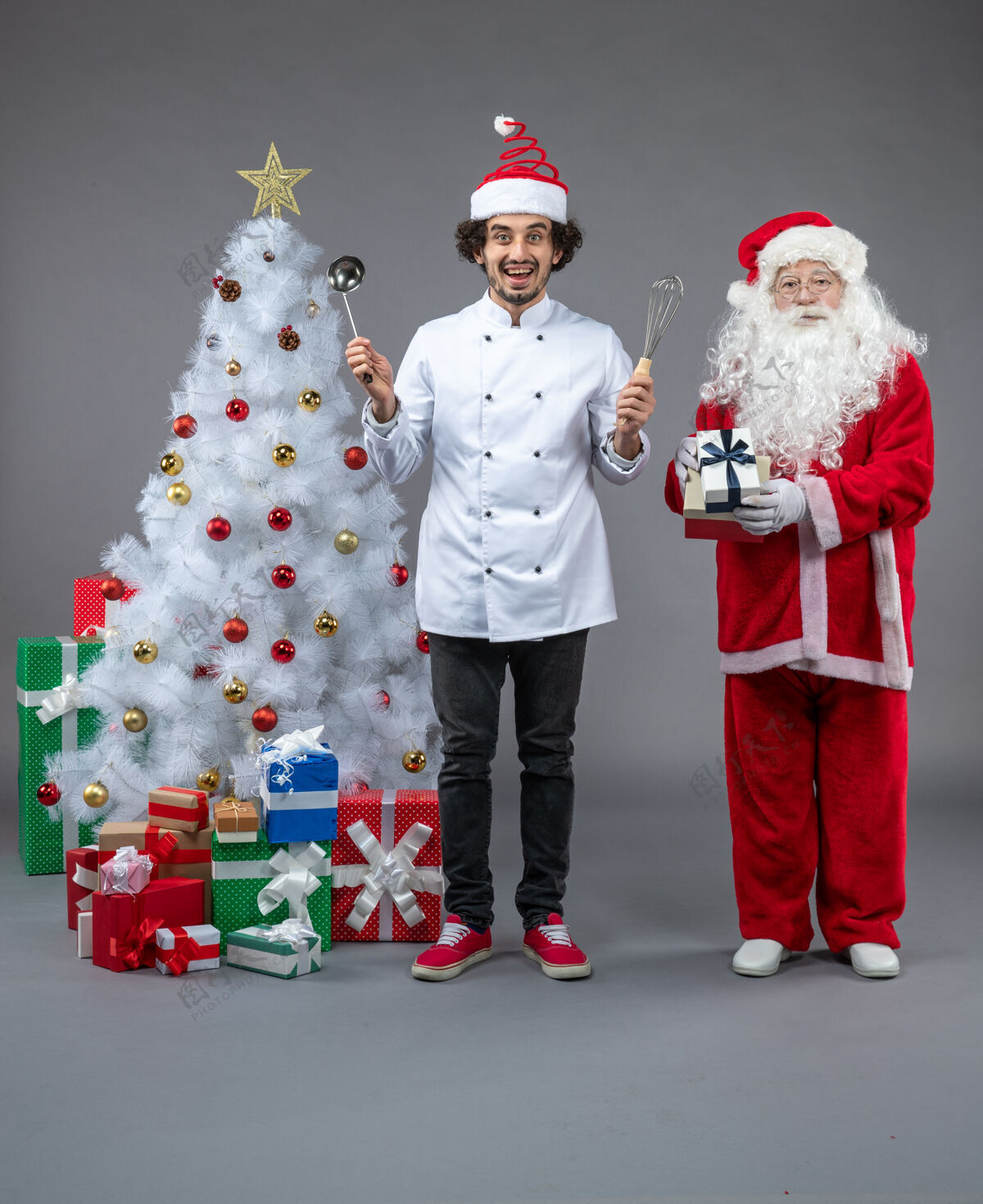 圣诞树圣诞老人和男厨师围着圣诞礼物在灰色墙上兴奋的前视图帽子圣诞树圣诞快乐