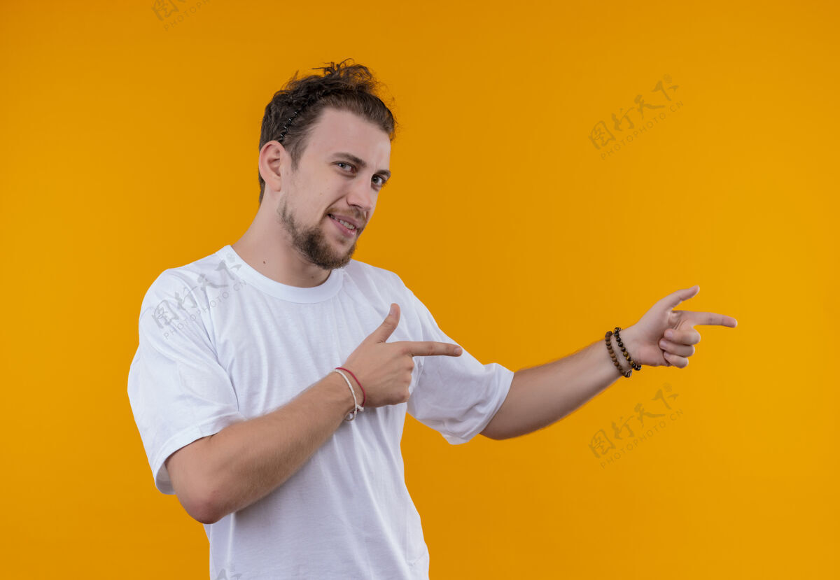 白色高兴的年轻人穿着白色t恤指向一边孤立的橙色背景男分橙色