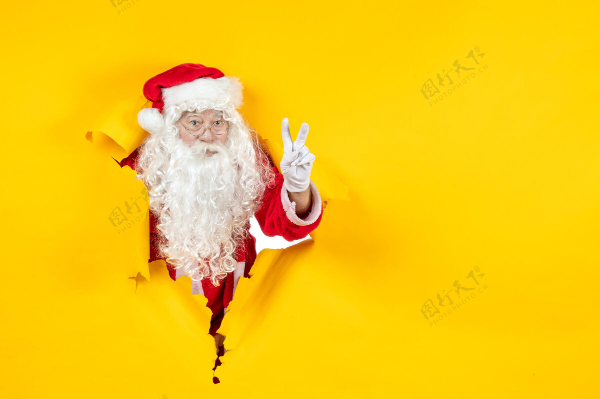 看圣诞老人透过撕破的纸黄色墙壁看的正视图纸圣诞老人前面