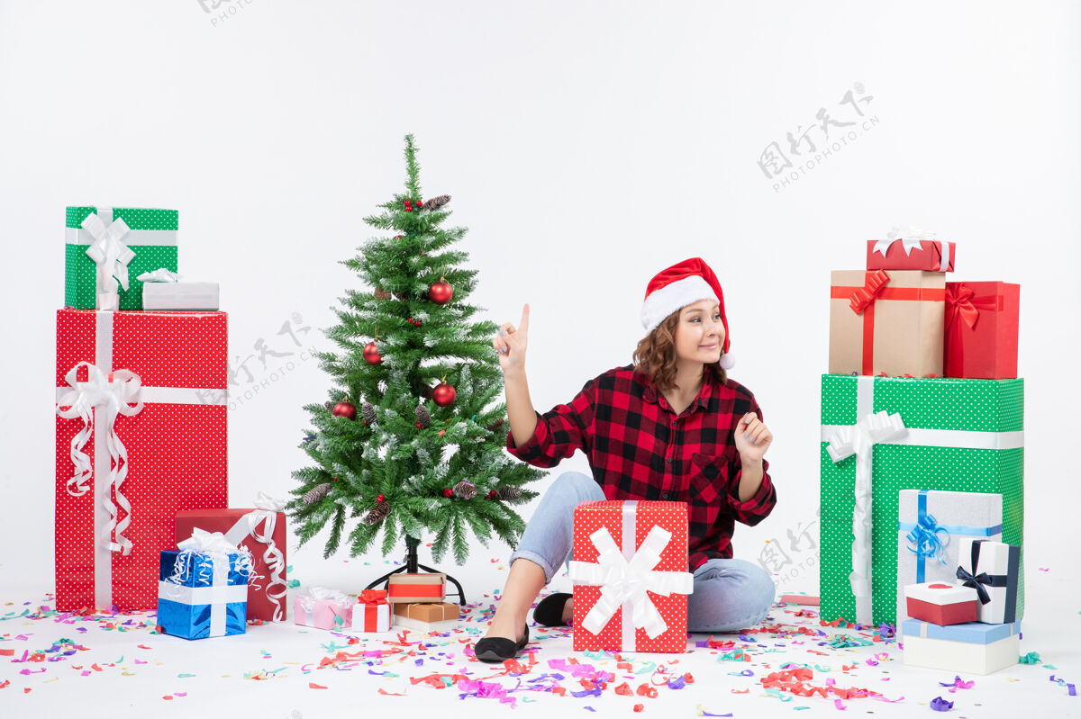圣诞快乐年轻女子围坐在礼物和白色墙上的小圣诞树前的视图节日前面人