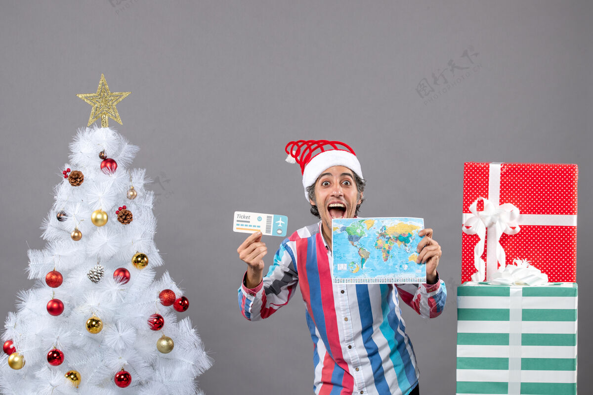 旅行正面图是一个戴着螺旋弹簧圣诞帽的帅哥 手里拿着世界地图和旅行票地图旅行者圣诞老人